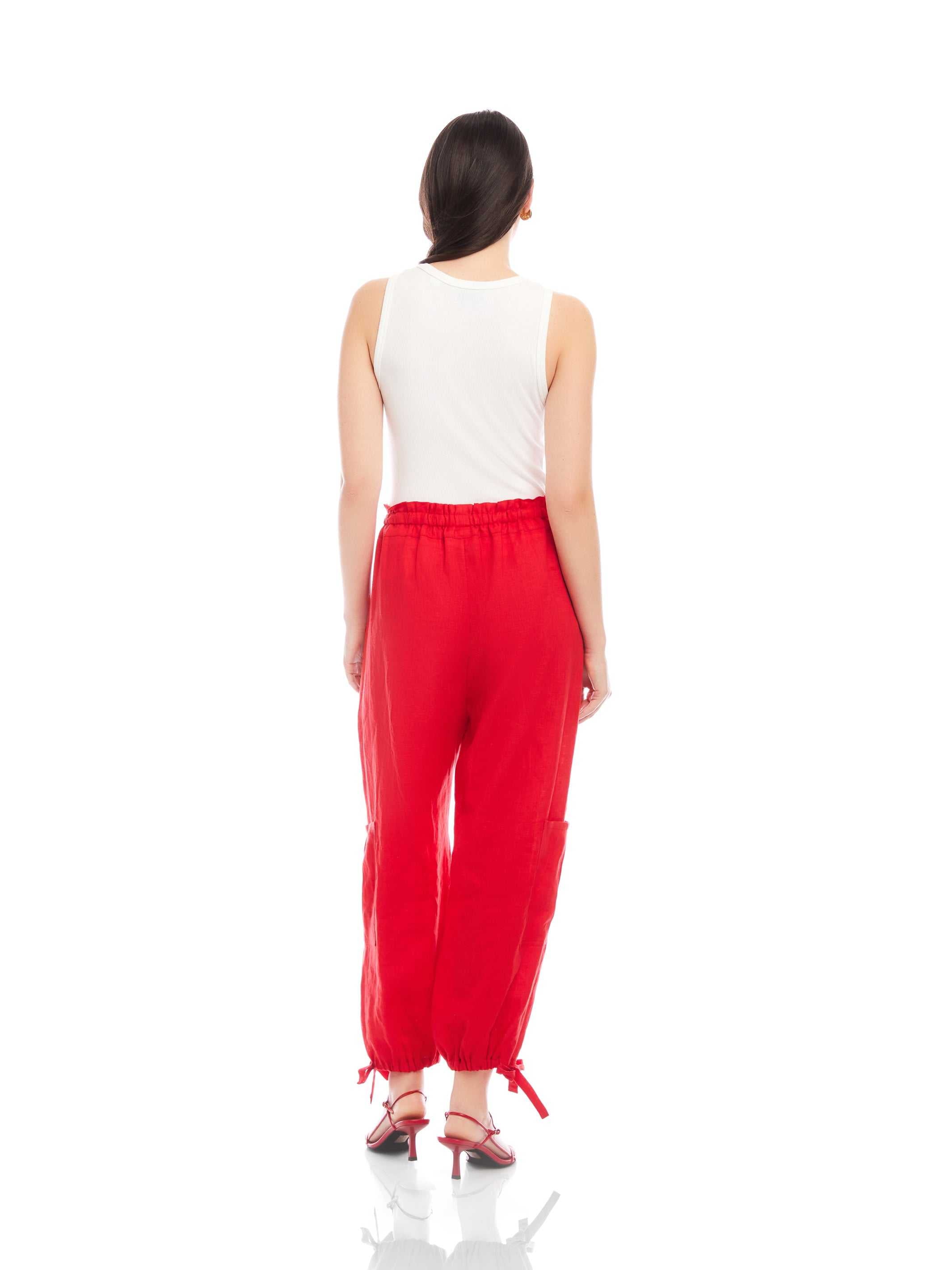 Woman wearing red Charo Cargo Pants with ankle drawstrings and side cargo pocket, paired with white sleeveless top.
