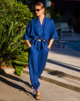 Woman wearing blue Charo Cargo Pants with ankle drawstrings and front pockets walking outdoors near a pool