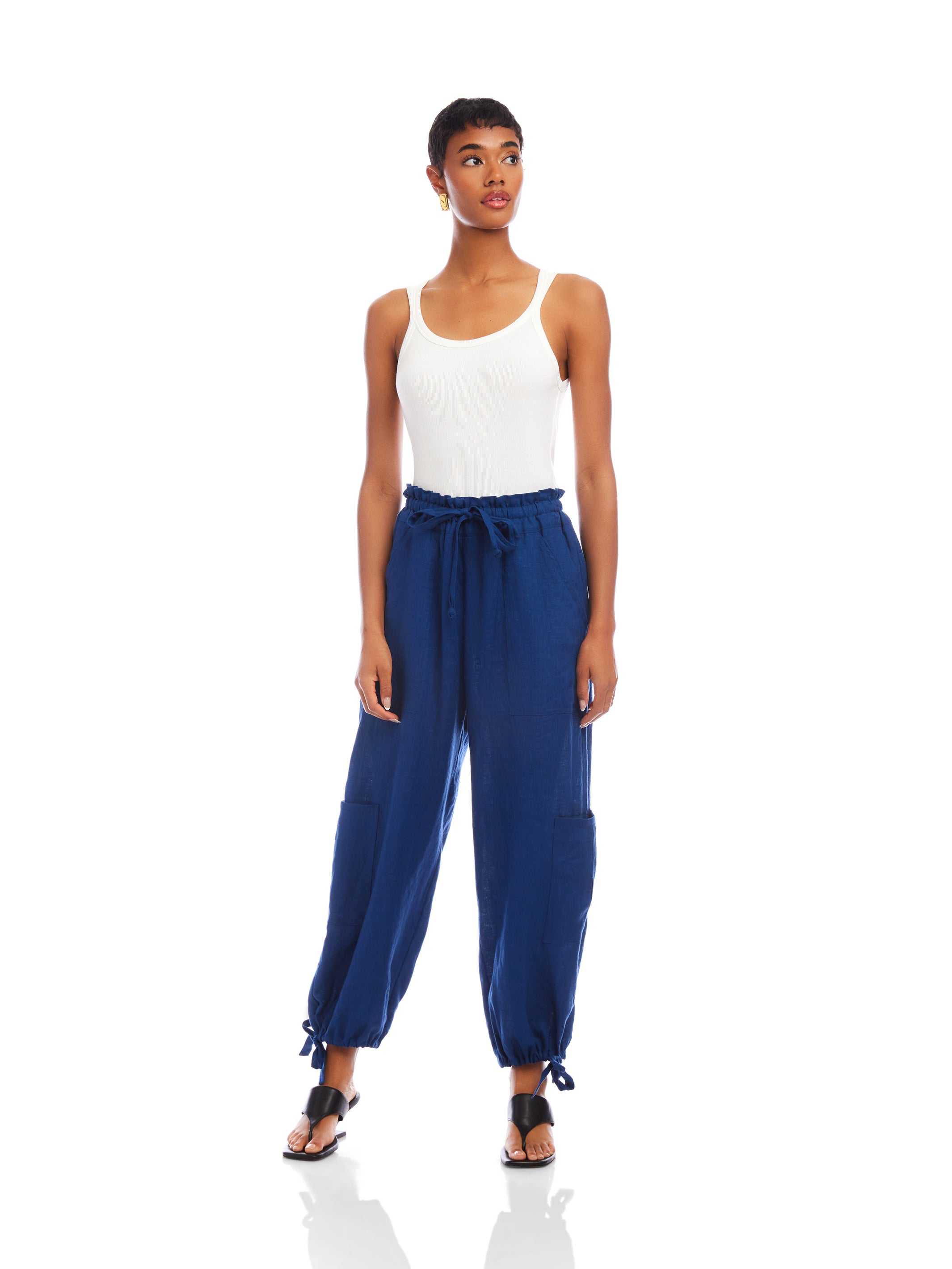 Woman wearing navy blue Charo Cargo Pants with ankle drawstrings and front and side pockets styled with white tank top and black sandals