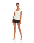 Woman wearing white Lorna Cap Sleeve Top with square neck and black shorts standing against white background