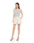 Woman wearing cream-colored Cassidy pleated shorts with front pleats and side pockets, paired with a striped sleeveless top and red heels.