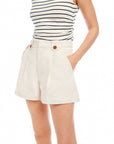 Woman wearing beige Cassidy Pleated Shorts with front pleats, side pockets, and button details paired with a striped sleeveless top