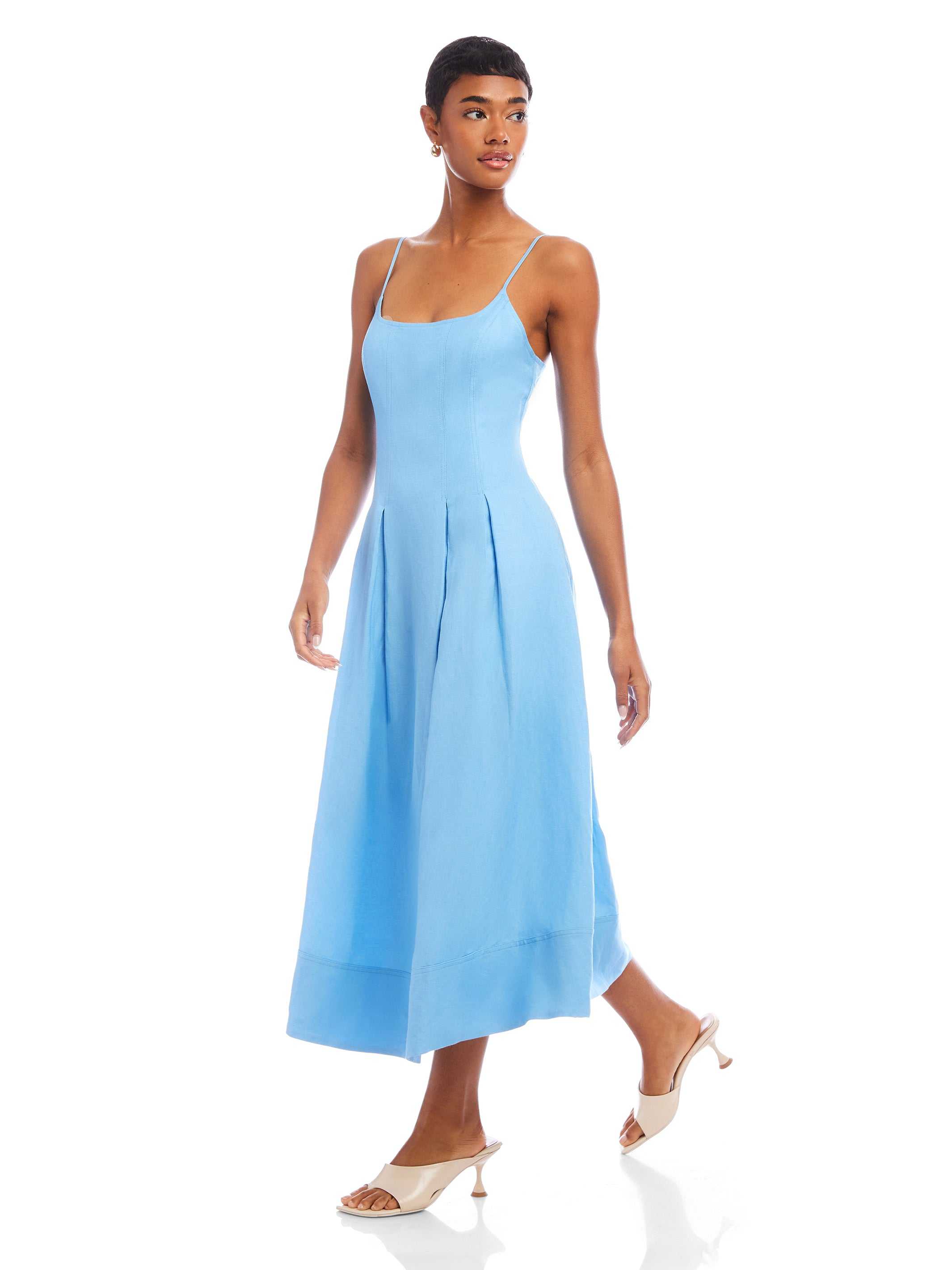 Woman wearing light blue Jessa Midi Dress with adjustable straps and scoop neck, featuring a flowy, sleeveless design and side pockets.
