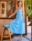 Woman wearing blue sleeveless Jessa Midi Dress with adjustable straps and side pockets in tropical setting