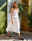 Woman wearing white Elsa Smocked Waist Midi Skirt with scalloped edges and smocked waist, styled with a matching top and black flats outdoors.