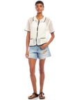 Woman wearing Gemma Crochet Shirt with contrast stitch crochet collar and pockets paired with distressed denim shorts and sandals