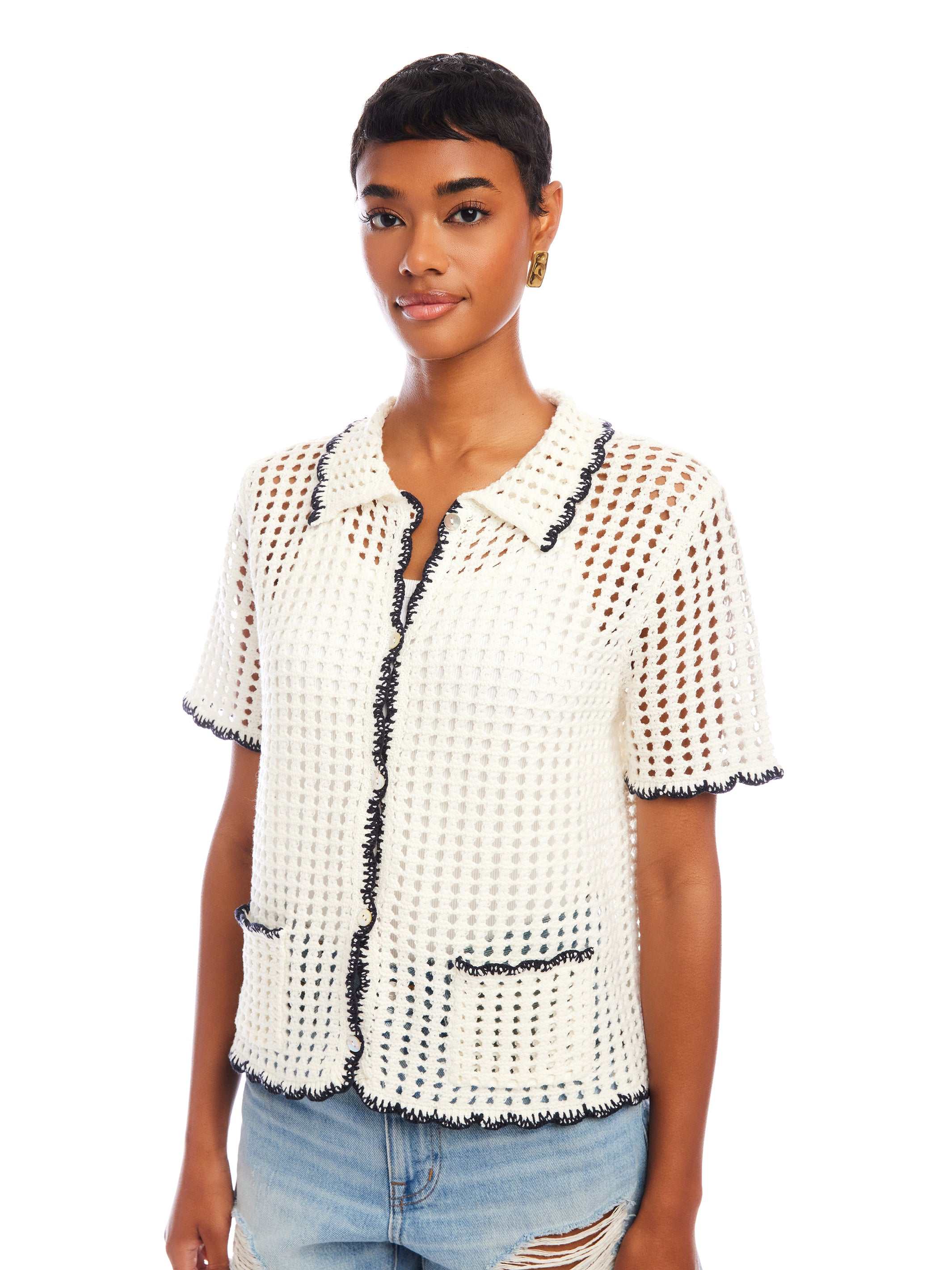 Woman wearing white Gemma Crochet Shirt with black trim, featuring short sleeves, crochet collar, and front pockets, paired with light blue ripped jeans