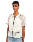 Woman wearing white Gemma Crochet Shirt with black trim, featuring short sleeves, crochet collar, and front pockets, paired with light blue ripped jeans
