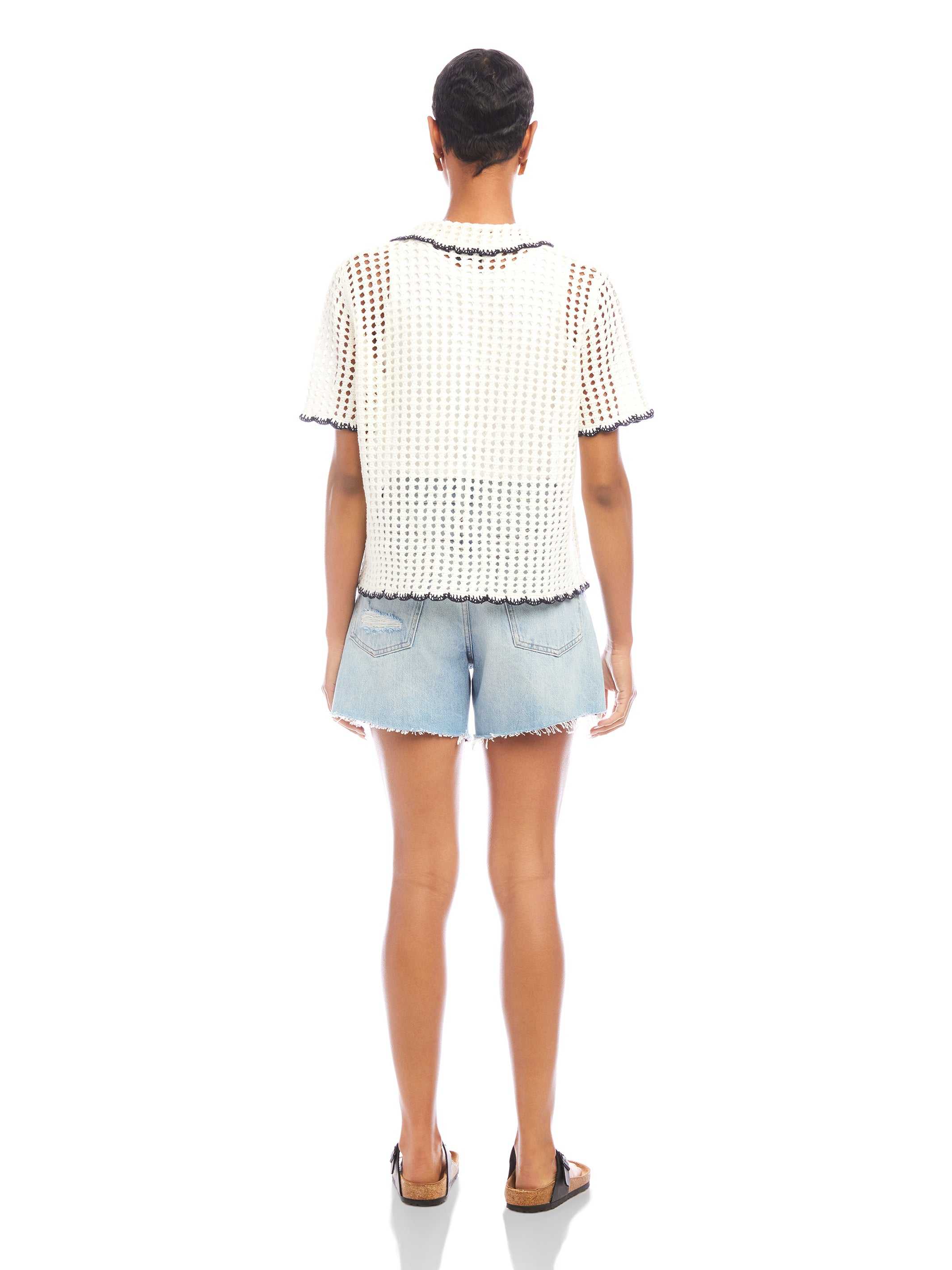 Back view of a person wearing a white Gemma Crochet Shirt with black trim and denim shorts