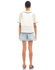 Back view of a person wearing a white Gemma Crochet Shirt with black trim and denim shorts