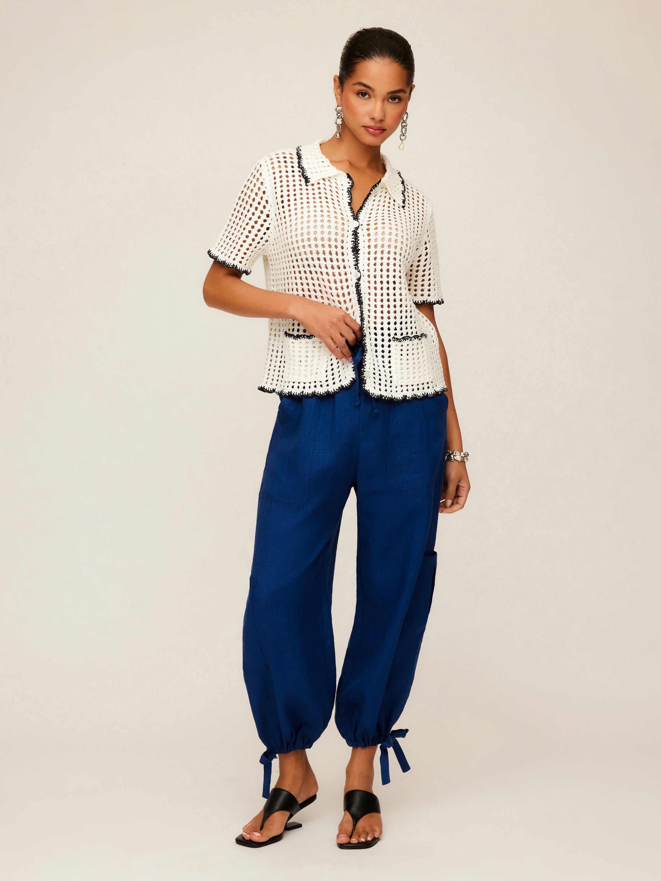 Woman wearing Gemma Crochet Shirt with contrast stitch, scalloped edge and two front pockets paired with blue pants and sandals