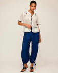 Woman wearing Gemma Crochet Shirt with contrast stitch, scalloped edge and two front pockets paired with blue pants and sandals