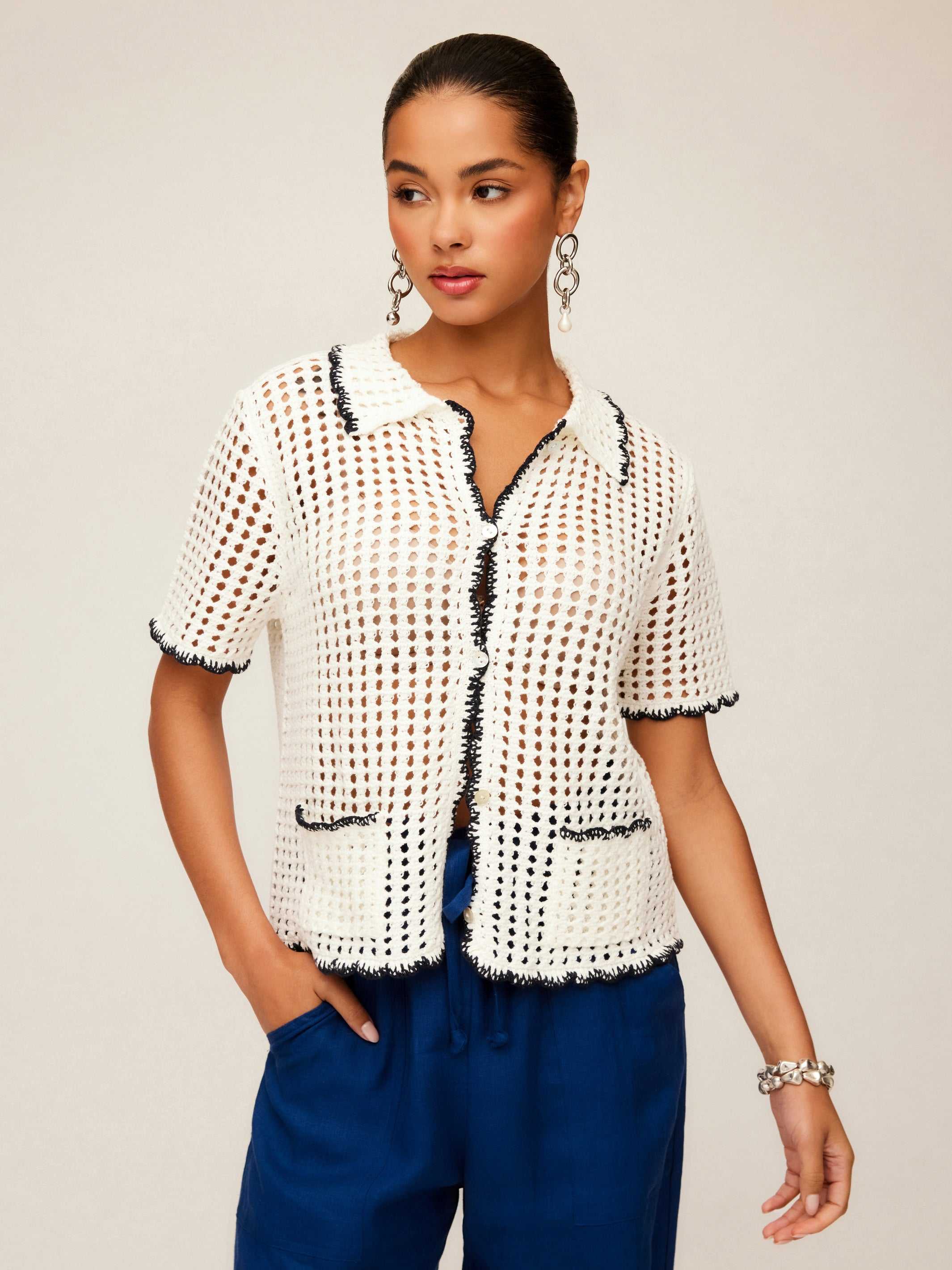 Woman wearing a white Gemma Crochet Shirt with contrast black stitch detailing, short sleeves, and front pockets paired with blue pants.