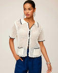 Woman wearing a white Gemma Crochet Shirt with contrast black stitch detailing, short sleeves, and front pockets paired with blue pants.