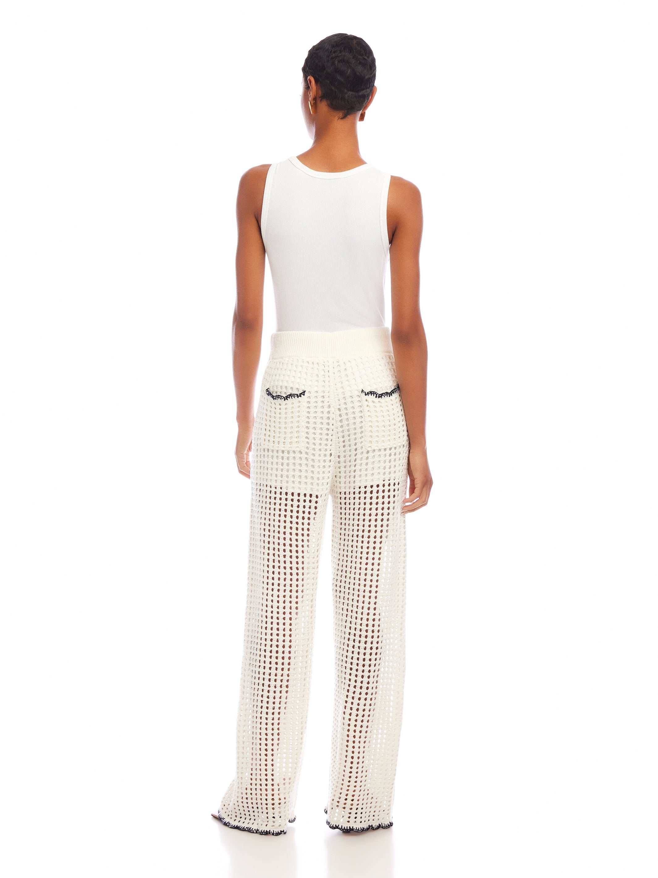 Woman wearing white Gianna crochet pants with contrast stitch, wide leg, scalloped edges, and back pockets, paired with a white sleeveless top, view from the back.