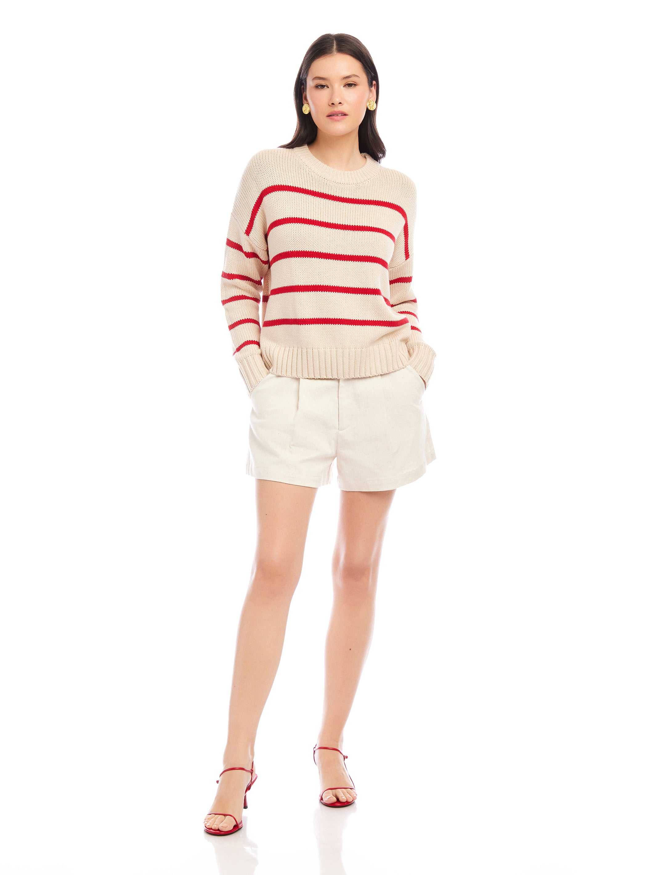 Woman wearing a Luca Crewneck Sweater with red stripes, drop shoulder sleeves, and ribbed cuffs, paired with white shorts and red sandals