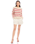 Woman wearing a Luca Crewneck Sweater with red stripes, drop shoulder sleeves, and ribbed cuffs, paired with white shorts and red sandals