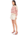 Woman wearing a Luca Crewneck Sweater with red stripes and loose fit paired with white shorts and red heels