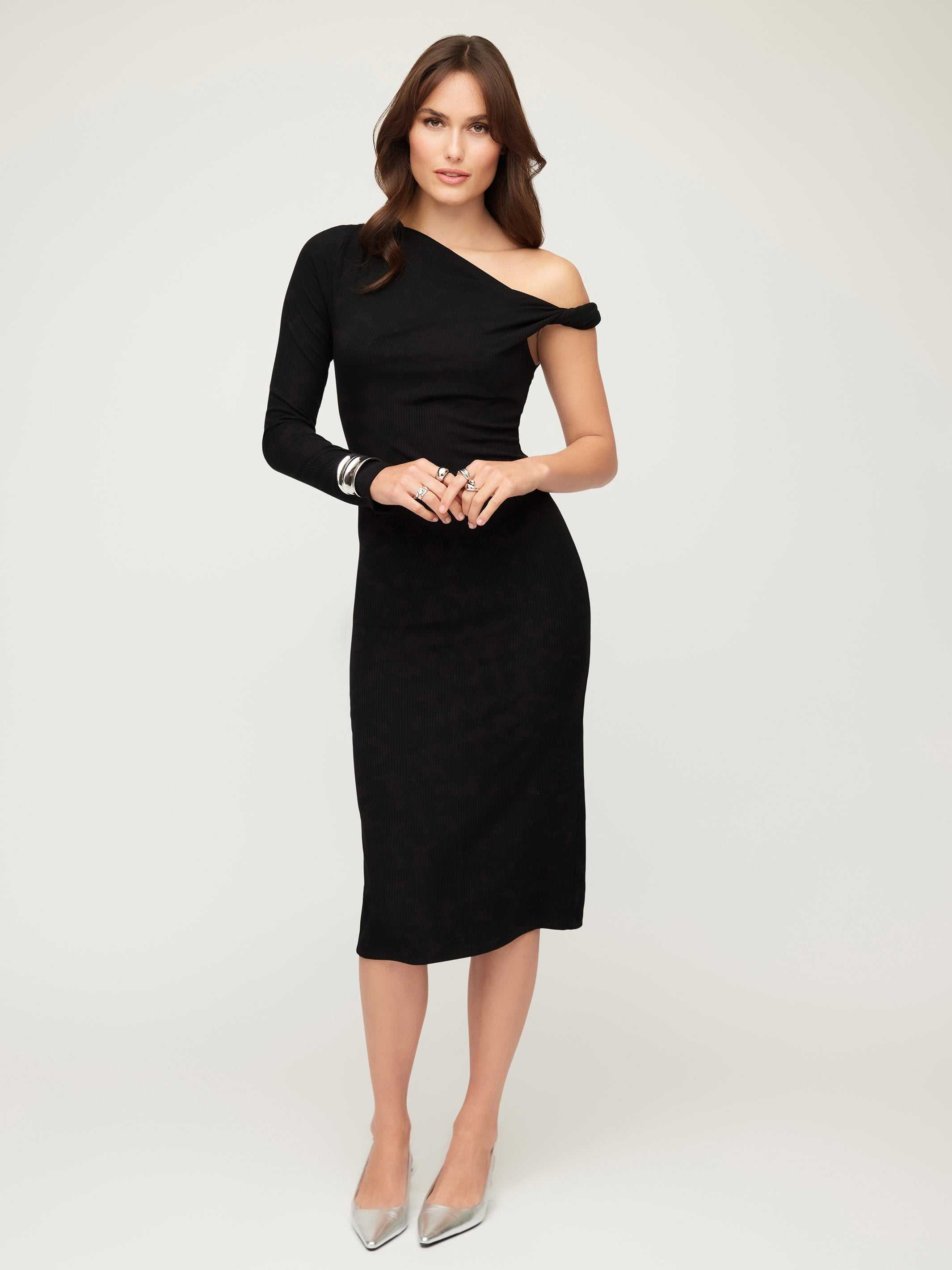 Model wearing black Nadia Dress with asymmetric neck and one long sleeve, fitted silhouette, and midi length.