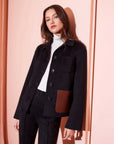 Black Ludlow Jacket with boxy fit, wool blend, contrast faux leather pocket, and button-down closure worn with black pants and white turtleneck.