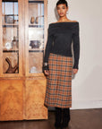 woman wearing Kaia Midi Skirt with plaid pattern and front slit, styled with off-shoulder black top and boots