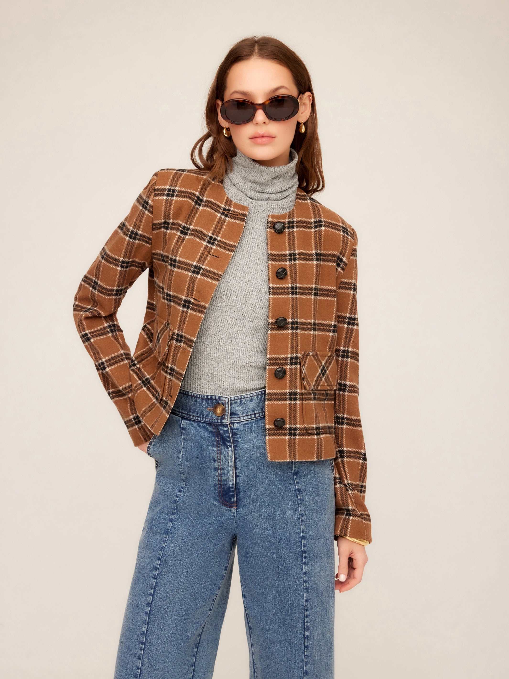 Woman wearing a cropped Jackie Micro Jacket in brown plaid with textured leather-effect buttons and a collarless neckline.