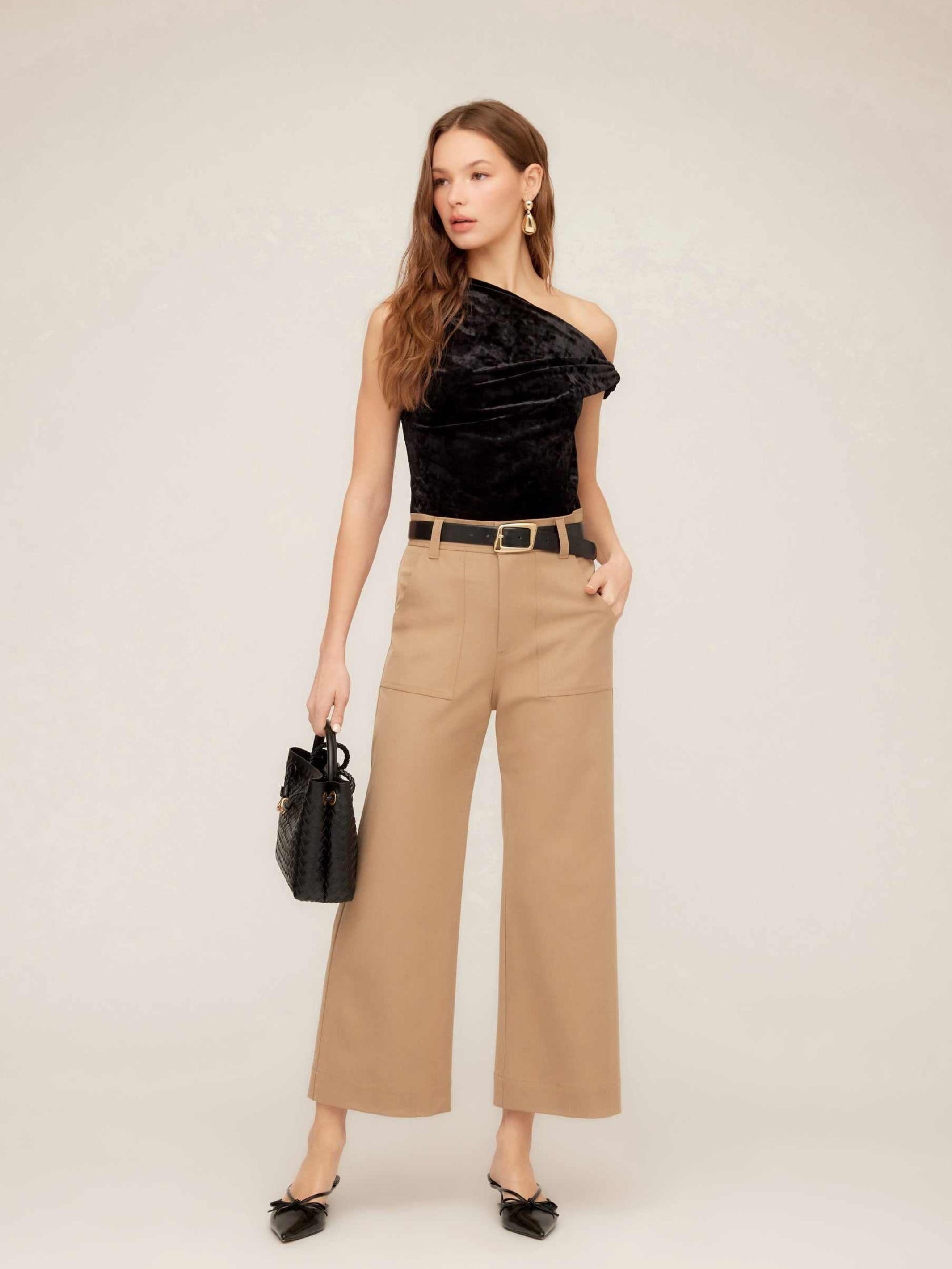 Woman wearing beige Rylee Crop Pants with wide-leg cropped fit, black belt, black one-shoulder top, and black handbag.