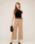 Woman wearing beige Rylee Crop Pants with wide-leg cropped fit, black belt, black one-shoulder top, and black handbag.