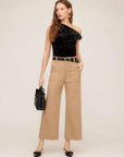 Woman wearing beige Rylee Crop Pants with wide-leg cropped fit, black belt, black one-shoulder top, and black handbag.