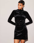Woman wearing black Beatrice Side-Shirred Dress made of stretch crushed velvet with turtleneck and long sleeves