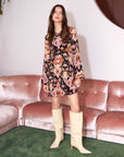Woman wearing a Layne Mini Dress with Byzantine print, long angled sleeves, split neck, and front slit, paired with cream knee-high boots.