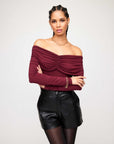 Woman wearing a burgundy Bella Off-The-Shoulder Top with long sleeves and shirring detail paired with black leather shorts
