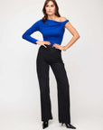 Woman wearing a blue Long Sleeve Nadia Top with off-the-shoulder asymmetrical drape neck and black pants