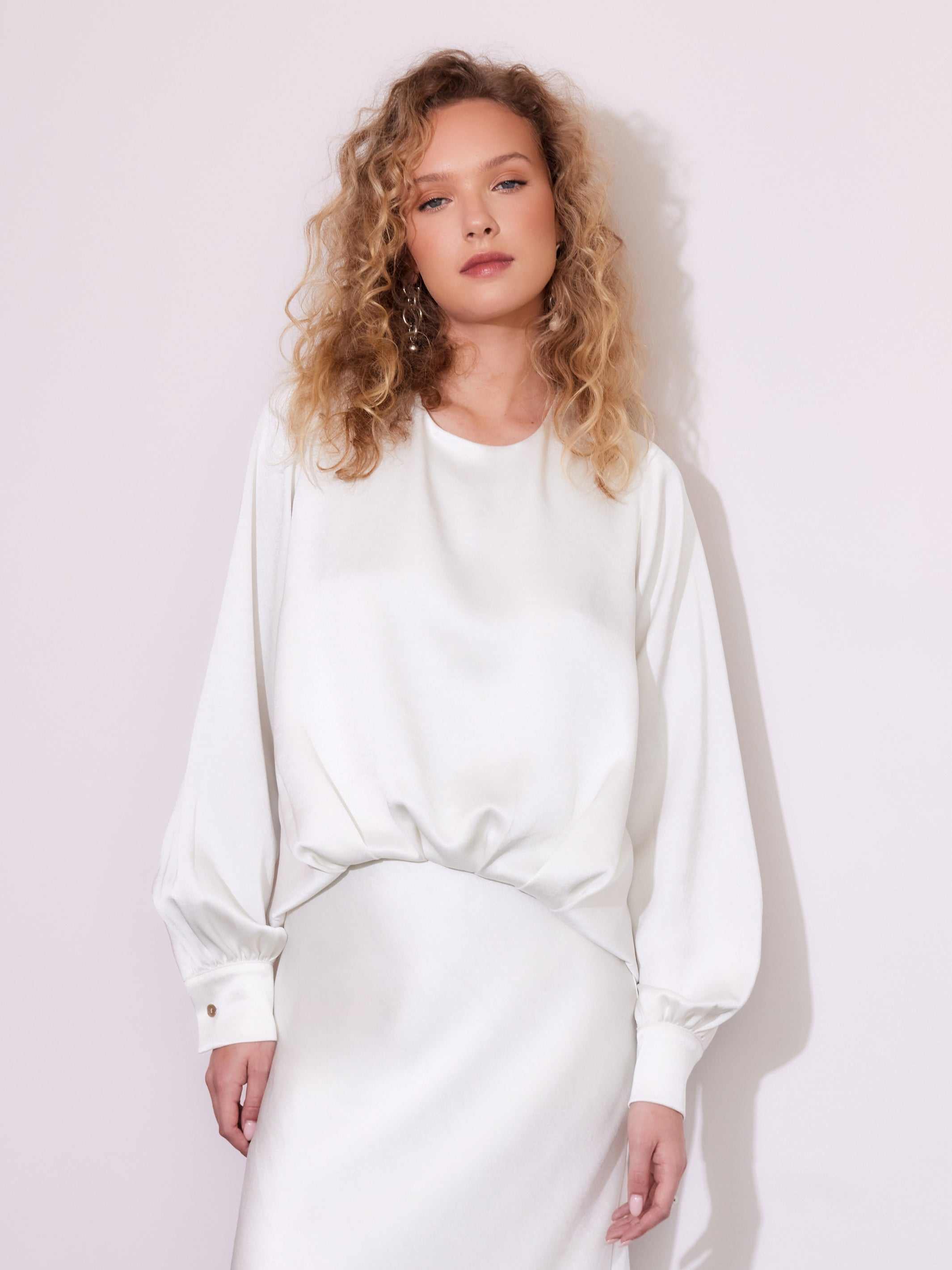 Woman wearing a white blouson satin top with long sleeves and crew neck, styled with a matching skirt.