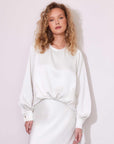 Woman wearing a white blouson satin top with long sleeves and crew neck, styled with a matching skirt.