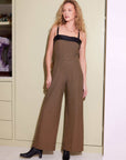 Woman wearing Paloma Jumpsuit with wide legs and houndstooth pattern, featuring contrast faux leather straps and square neckline.