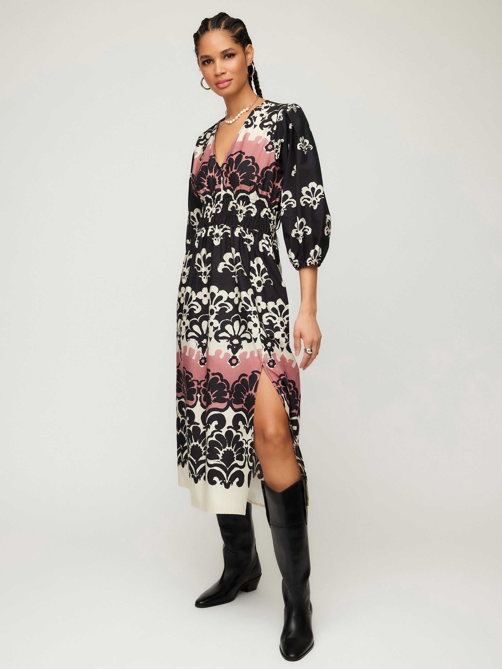 Woman wearing Lizbeth Shirred Waist Dress with damask block print, V-neck, 3/4 bishop sleeves, side slit, and pockets paired with black boots.