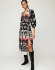 Woman wearing Lizbeth Shirred Waist Dress with damask block print, V-neck, 3/4 bishop sleeves, side slit, and pockets paired with black boots.