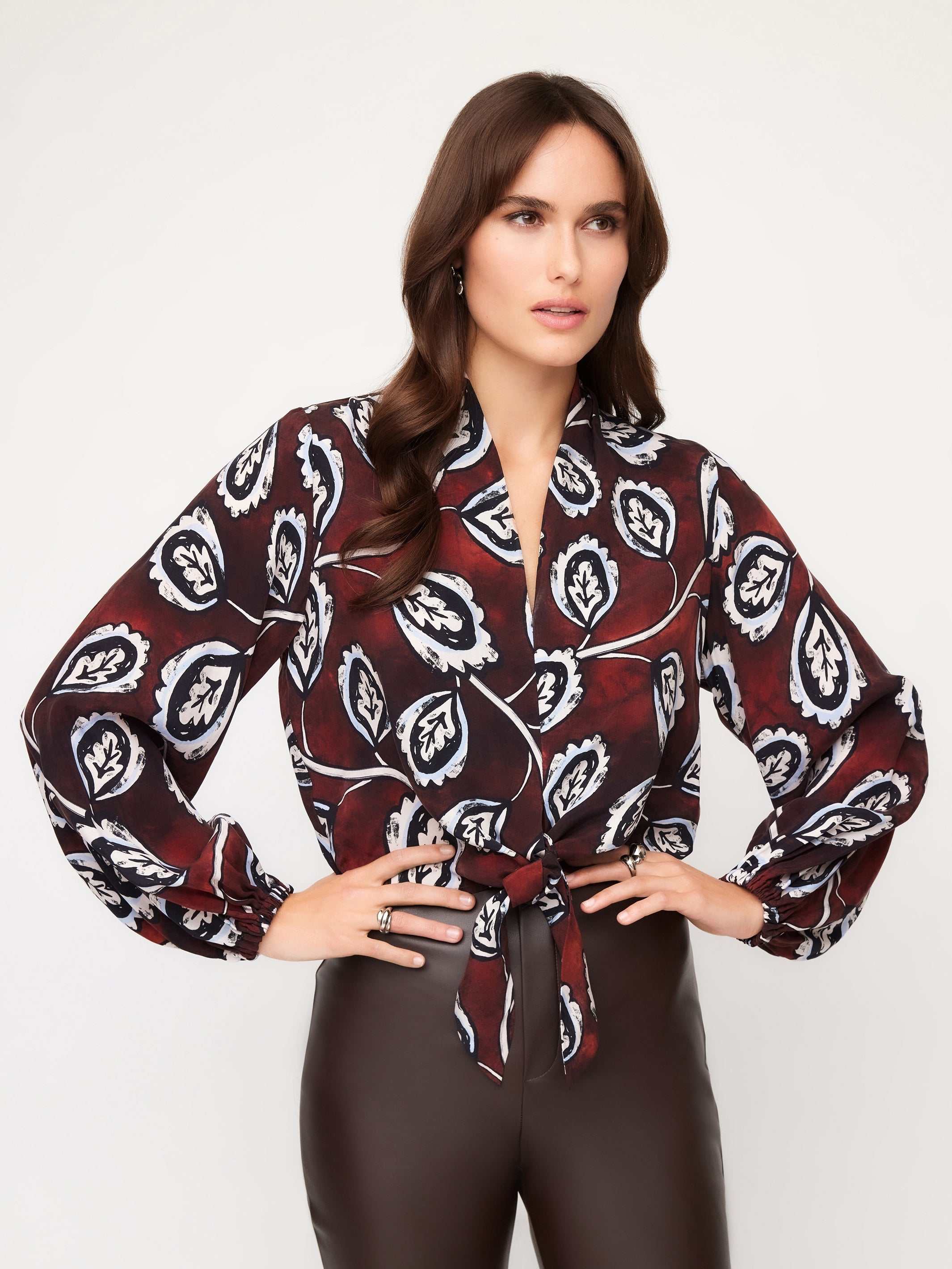 Woman wearing a scarlet tie-front top with long blouson sleeves and floral stamp print paired with high rise pants