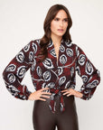 Woman wearing a scarlet tie-front top with long blouson sleeves and floral stamp print paired with high rise pants