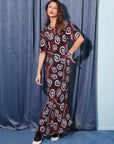 Woman wearing a fitted Stila midi dress with floral stamp print, short sleeves, and keyhole back closure standing against a blue curtain background.