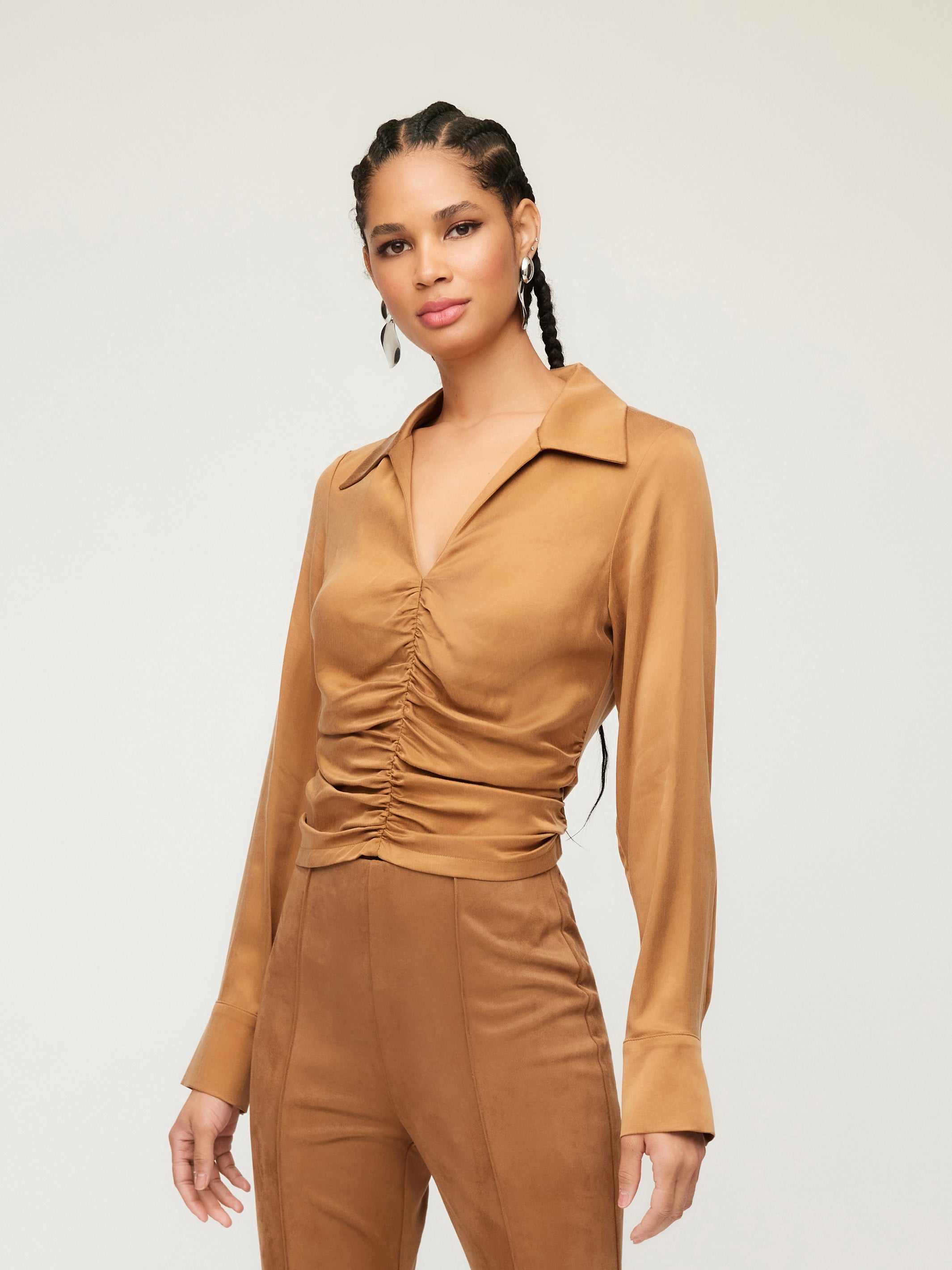 Woman wearing a brown Arabella Shirred Top with collared V-neck and cuffed long sleeves.