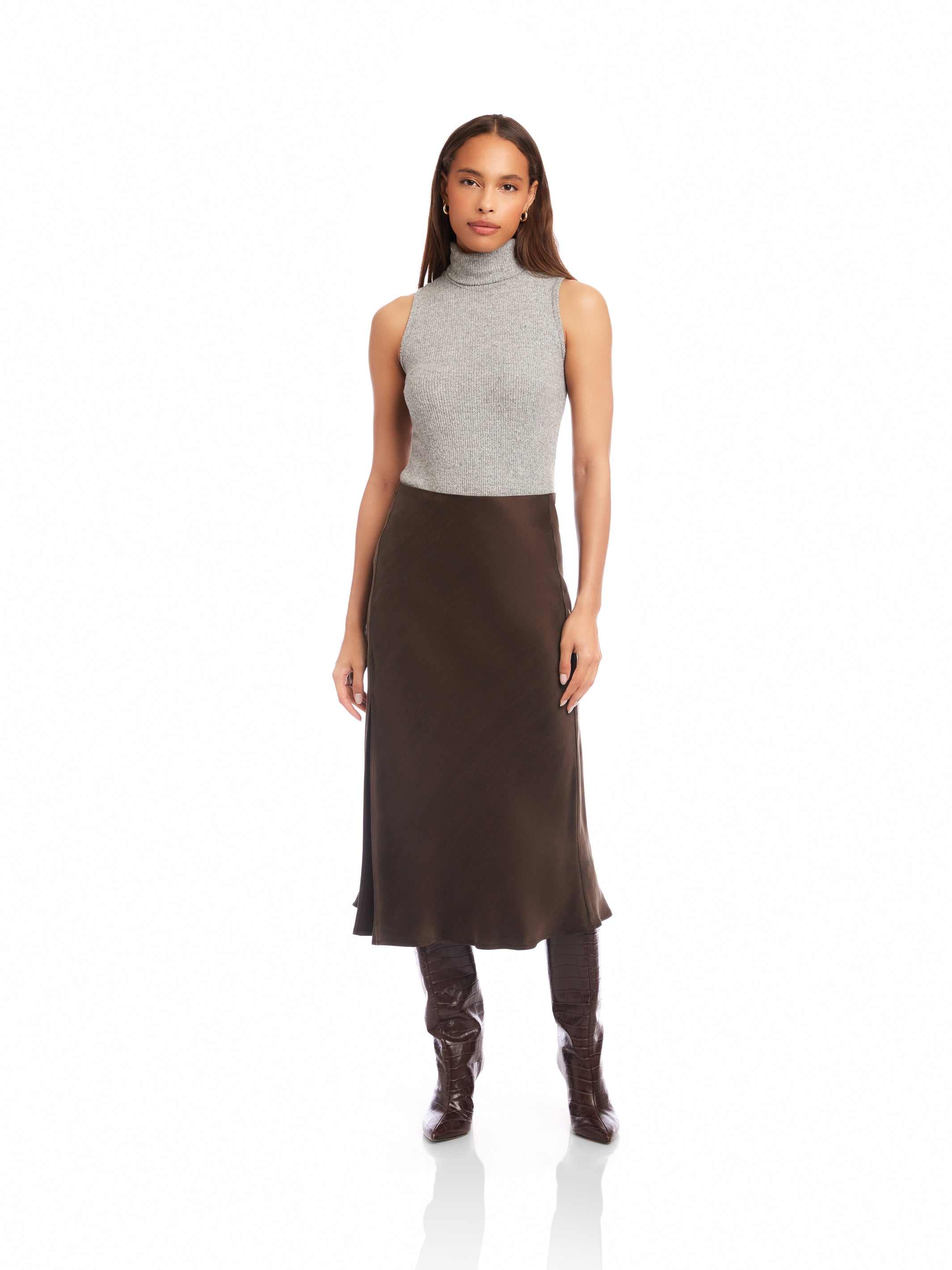 Woman wearing Brielle Midi Skirt in dark brown cupro fabric with high side slit and elastic waist, paired with grey sleeveless turtleneck and boots