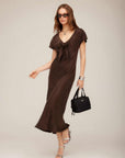 Woman wearing brown Emmeline Tie-Front Bias Dress with deep V-neck and flutter sleeves carrying black handbag