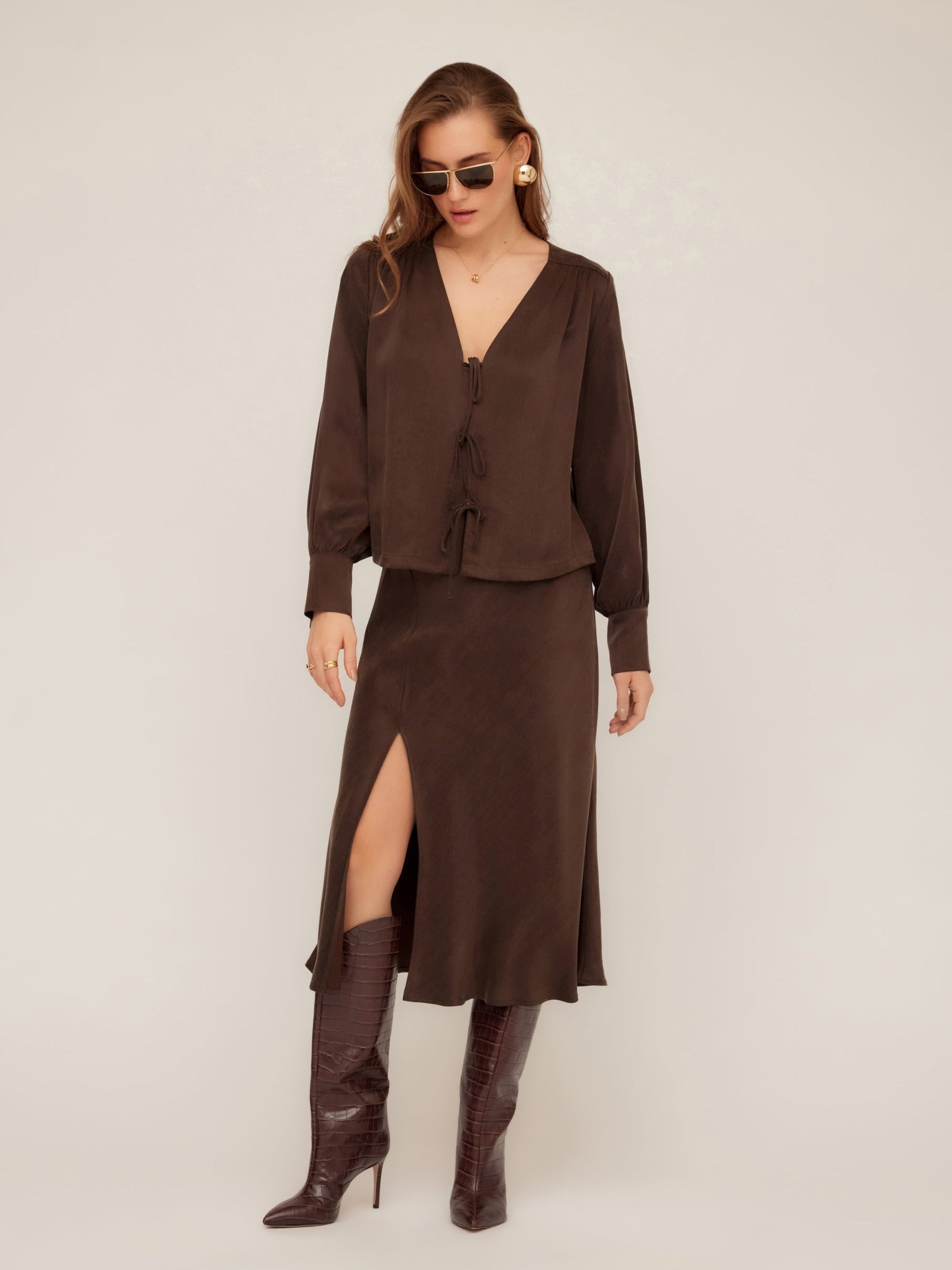 Woman wearing Brielle Midi Skirt in brown cupro fabric with side slit and elastic waist paired with matching top and brown boots