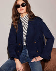 Woman wearing navy blue Chelsea Cropped Trench Jacket with tortoiseshell buttons and shoulder epaulets over striped turtleneck and jeans