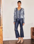 Woman wearing navy Sigourney Pintuck Pants made of faux leather with flared cropped legs and front pintuck seams.