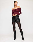 Woman wearing black high-waist modern faux leather shorts with side pockets and a burgundy off-shoulder top