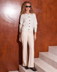Woman wearing cream Finley Wide-Leg Pants with buttoned sweater and sunglasses standing on stairs against brown wall