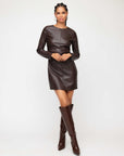 Woman wearing a brown faux leather Ziggy mini dress with long sleeves and crew neck paired with matching knee-high boots